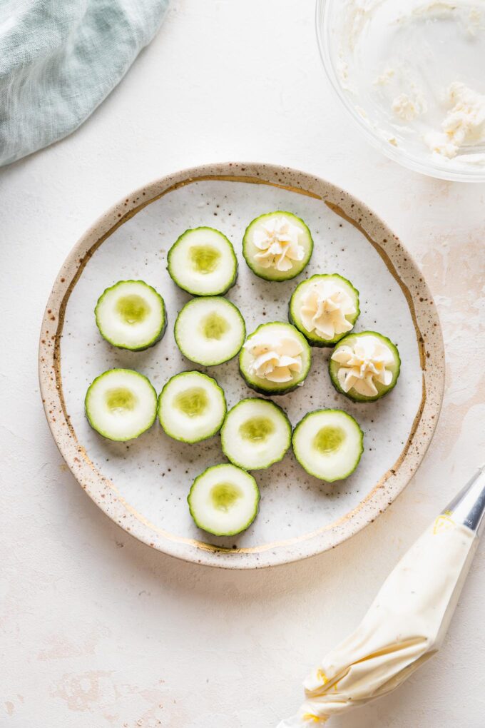 A piping bag filled with Boursin cheese being used to fill cucumber slices for an appetizer.