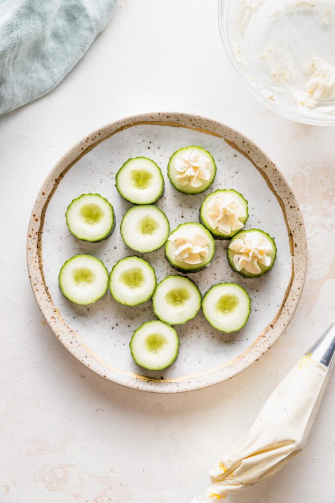 A piping bag filled with Boursin cheese being used to fill cucumber slices for an appetizer.