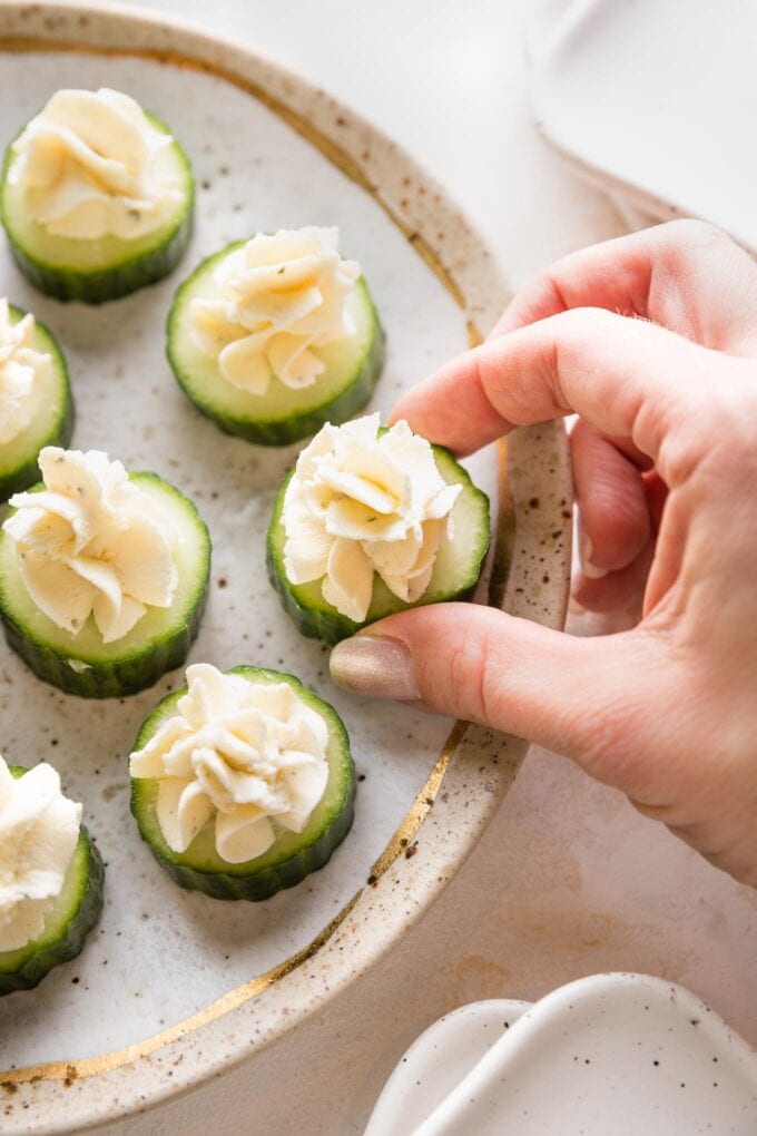 Close up of a hand picking up a cucumber Boursin appetizer off a plate.