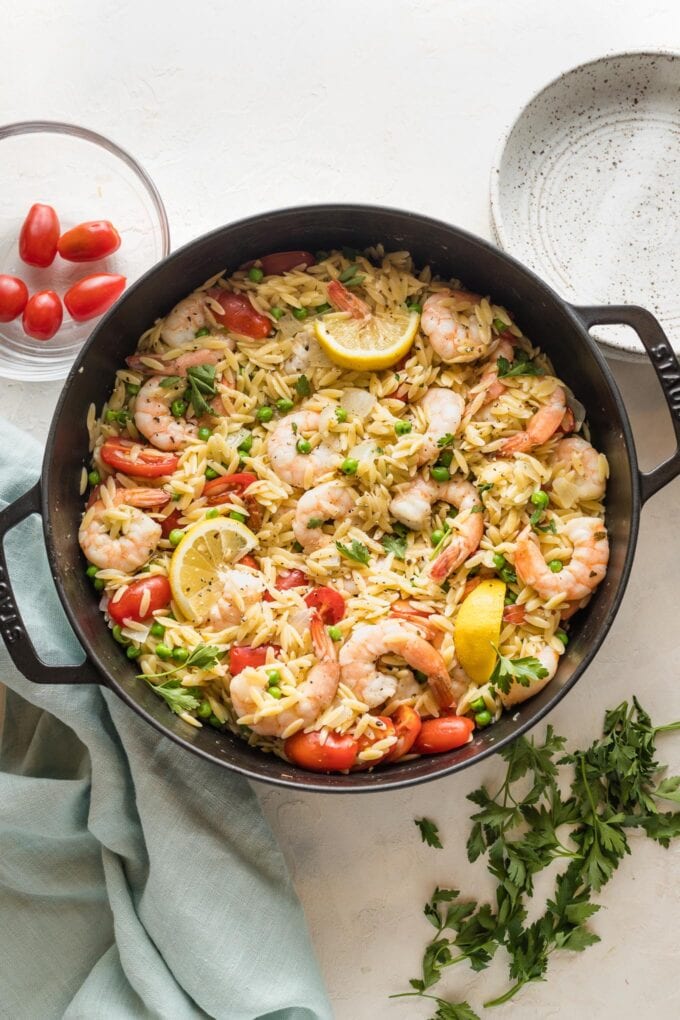 Large cast iron skillet filled with a one pot meal of lemon shrimp orzo with peas and tomatoes.