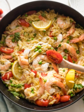Close up of a serving spoon lifting a helping of lemon shrimp orzo out of a cast iron skillet.