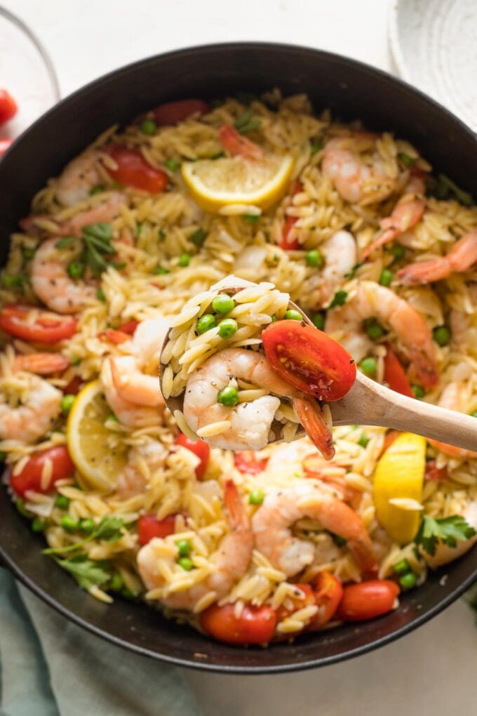 Close up of a serving spoon lifting a helping of lemon shrimp orzo out of a cast iron skillet.
