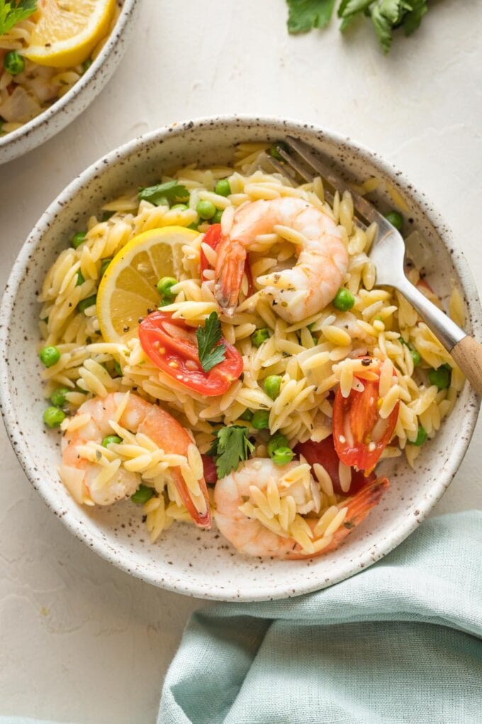 Bowl of lemon shrimp orzo with peas and tomatoes, served and ready to dive in with a fork.