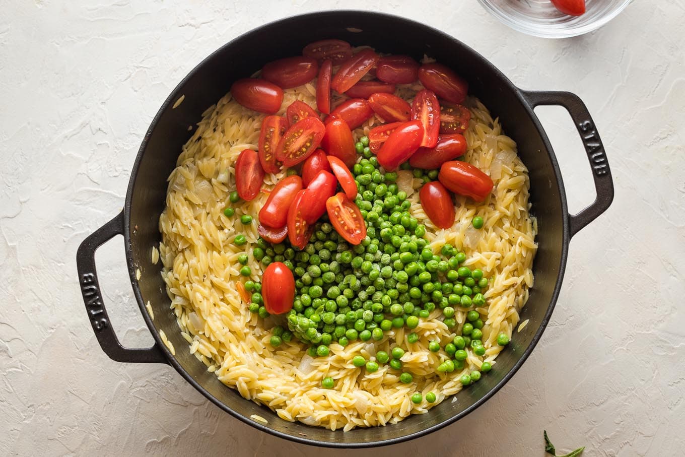 Cherry tomatoes and frozen peas added to cooked orzo.