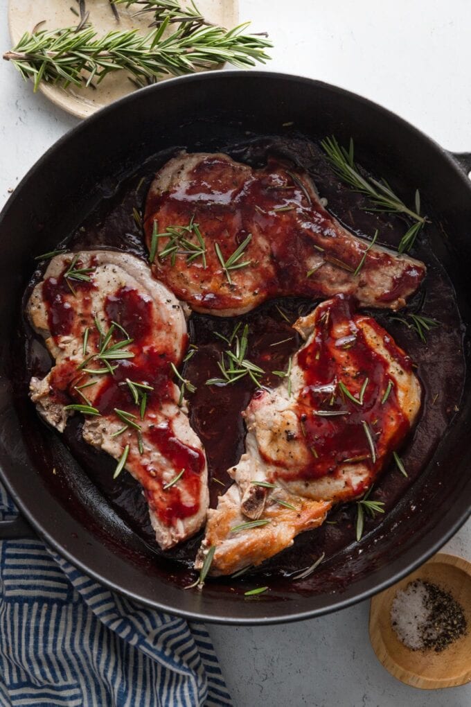 Large cast iron skillet with pork chops nestled in a balsamic plum sauce with fresh rosemary.