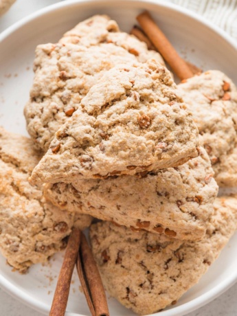 Close up of a cinnamon scone with cinnamon chips on a white plate.