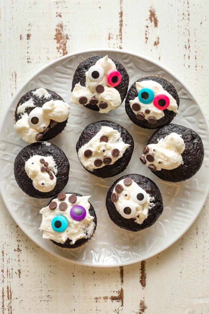 Plate of chocolate cupcakes with messy white frosting and decorations.