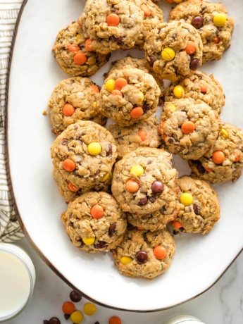 Reese's monster cookies arranged on a white tray, with glasses of milk nearby.