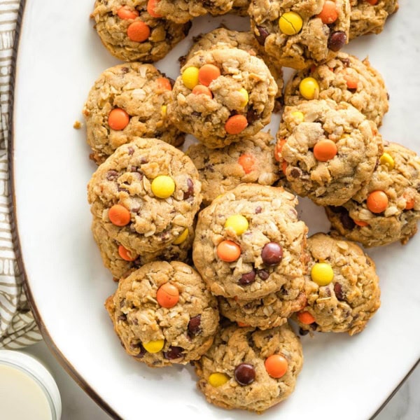Reese's monster cookies arranged on a white tray, with glasses of milk nearby.