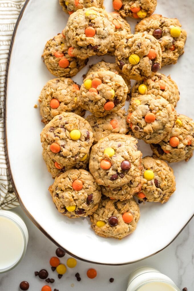 Reese's monster cookies arranged on a white tray, with glasses of milk nearby.