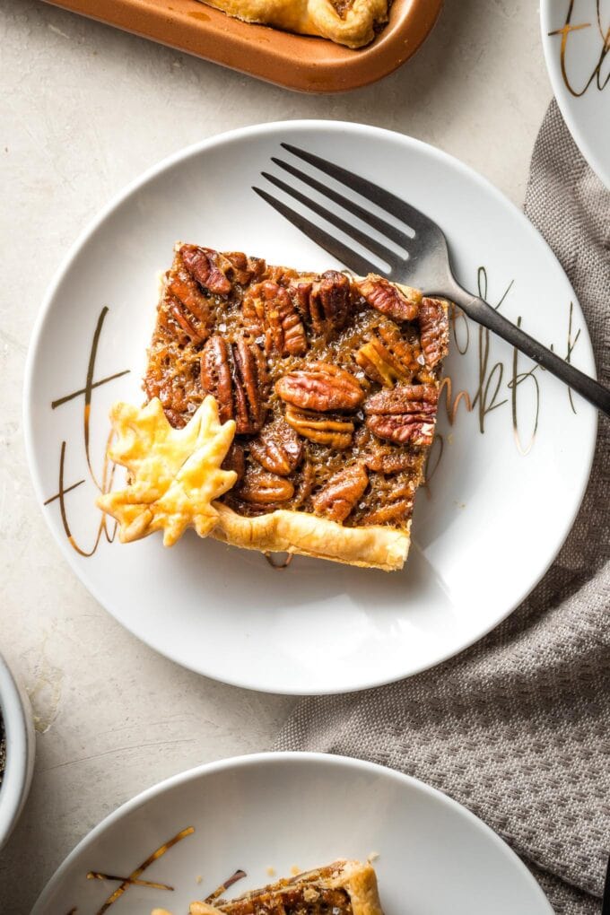 Close-up of a slice of slab pecan pie on a white plate with a fork.