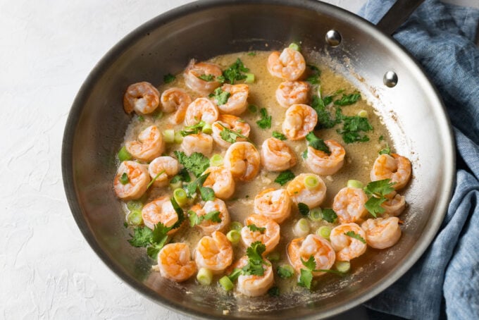 Shrimp cooking in a skillet with citrus butter sauce.