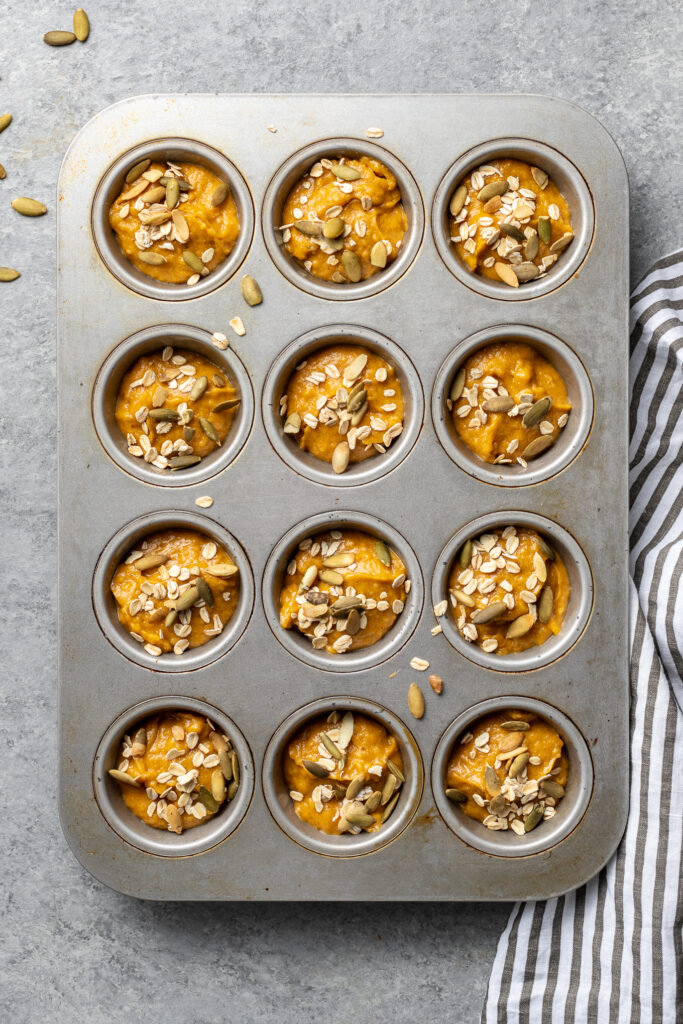 A muffin tin filled with batter for a batch of pumpkin muffins.