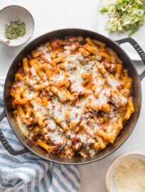 Overhead view of a cast iron skillet baked ziti garnished with Parmesan and dried parsley flakes.