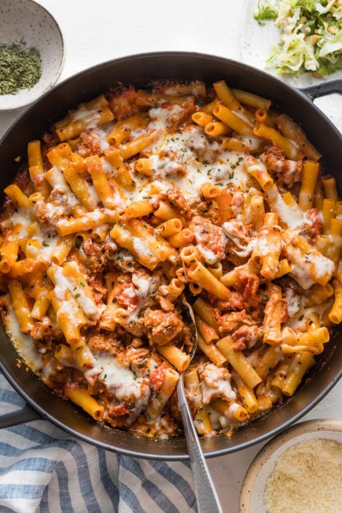 Large cast iron skillet filled with baked ziti with Italian sausage, ready to serve.