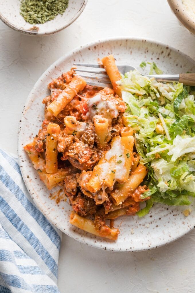 Small plate with a serving of baked ziti and Caesar salad.