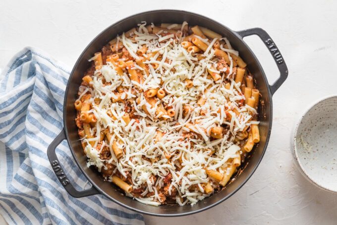 Shredded mozzarella sprinkled on top of a pasta dish, ready to bake.