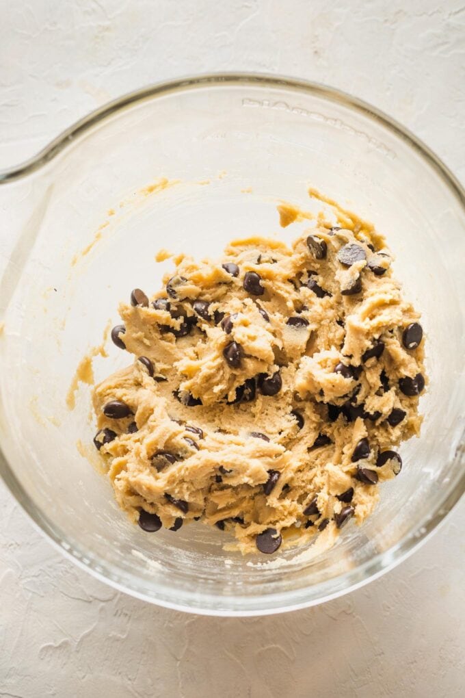 Close up of dough for bakery style chocolate chip cookies in a clear glass mixing bowl.