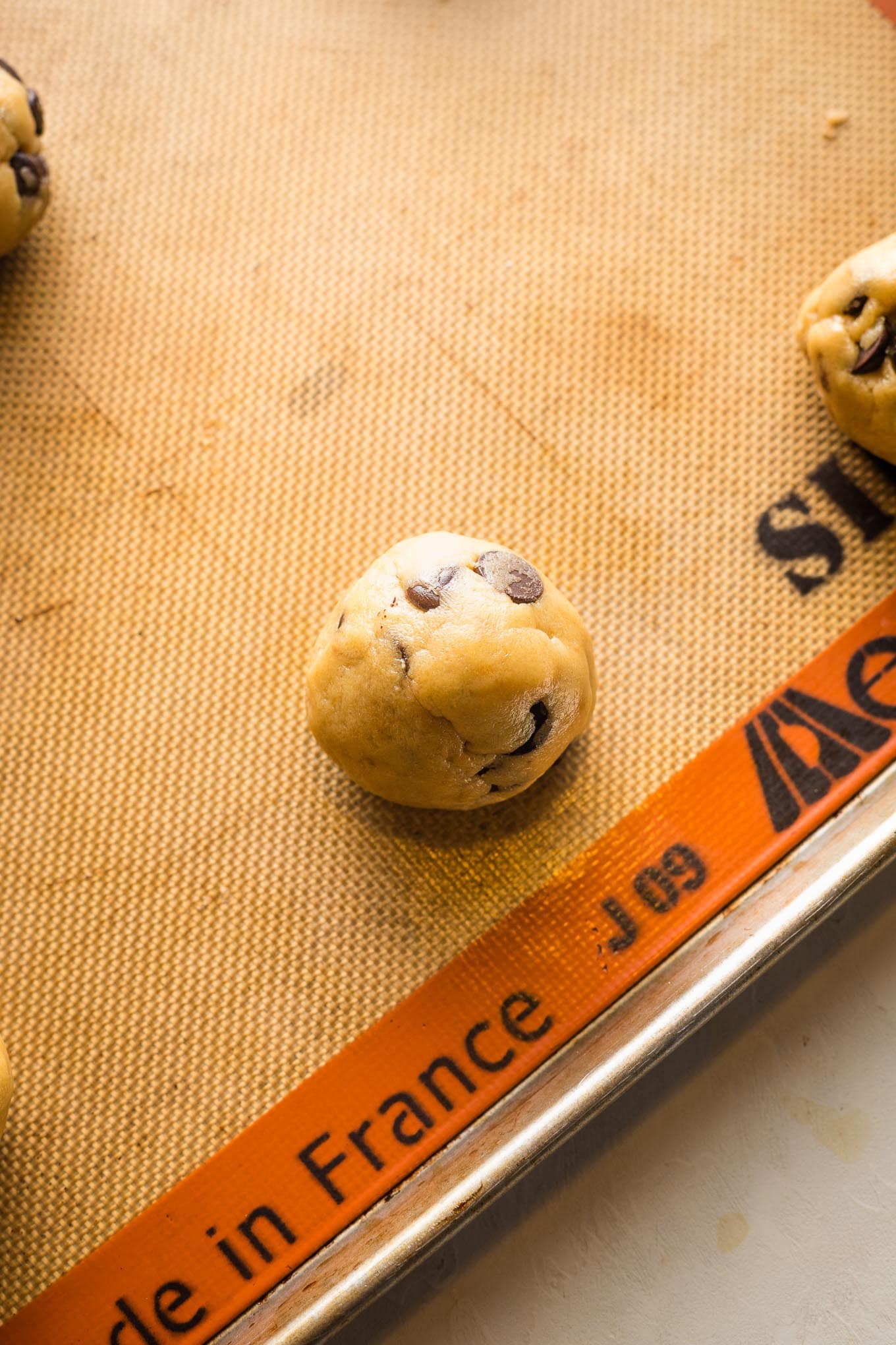 Close up of a large ball of cookie dough on a baking sheet lined with a silicone mat.