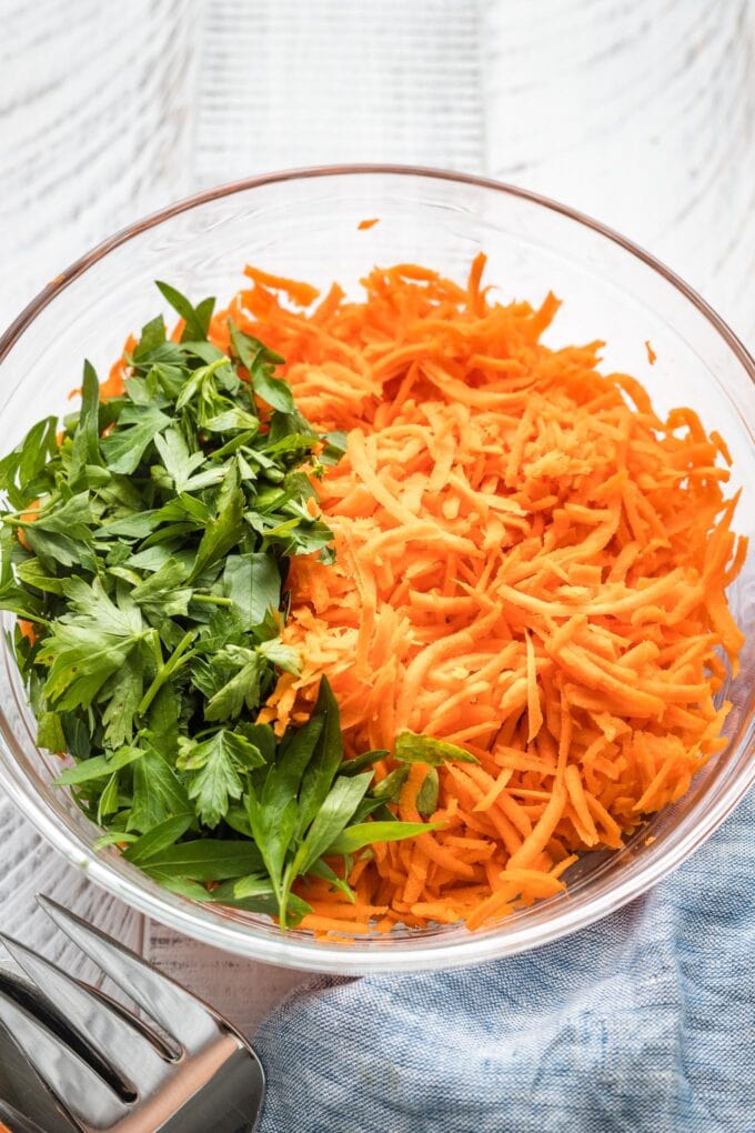 Close up of shredded carrots and chopped parsley in a clear prep bowl.