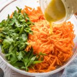 Salad dressing being poured onto a grated carrot salad.