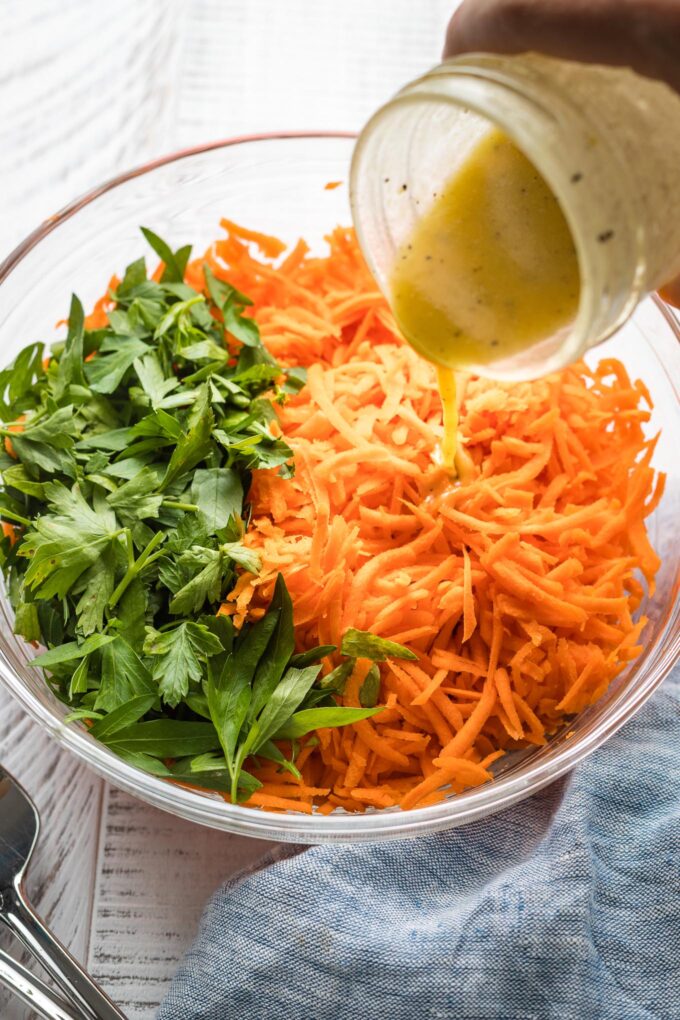 Salad dressing being poured onto a grated carrot salad.