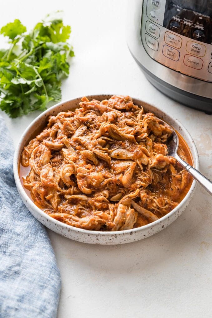 Serving bowl full of chicken Tinga with an Instant Pot and fresh cilantro in the background.