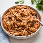 Serving bowl full of Instant Pot chicken Tinga with a smoky tomato sauce.