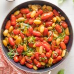 Large skillet full of pan fried gnocchi with roasted cherry tomatoes, fresh basil, and pine nuts.