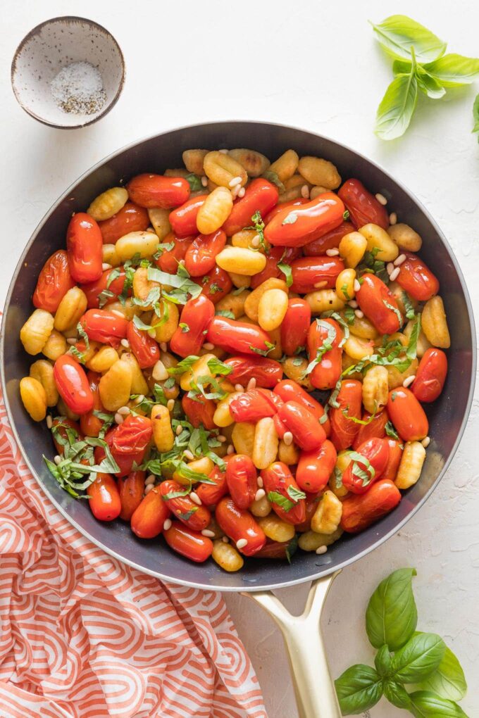 Large skillet full of pan fried gnocchi with roasted cherry tomatoes, fresh basil, and pine nuts.