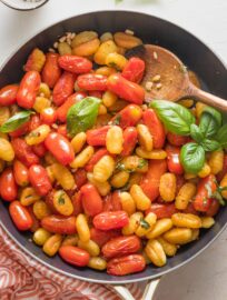 Serving spoon scooping out a portion of pan fried gnocchi with roasted cherry tomatoes and basil.