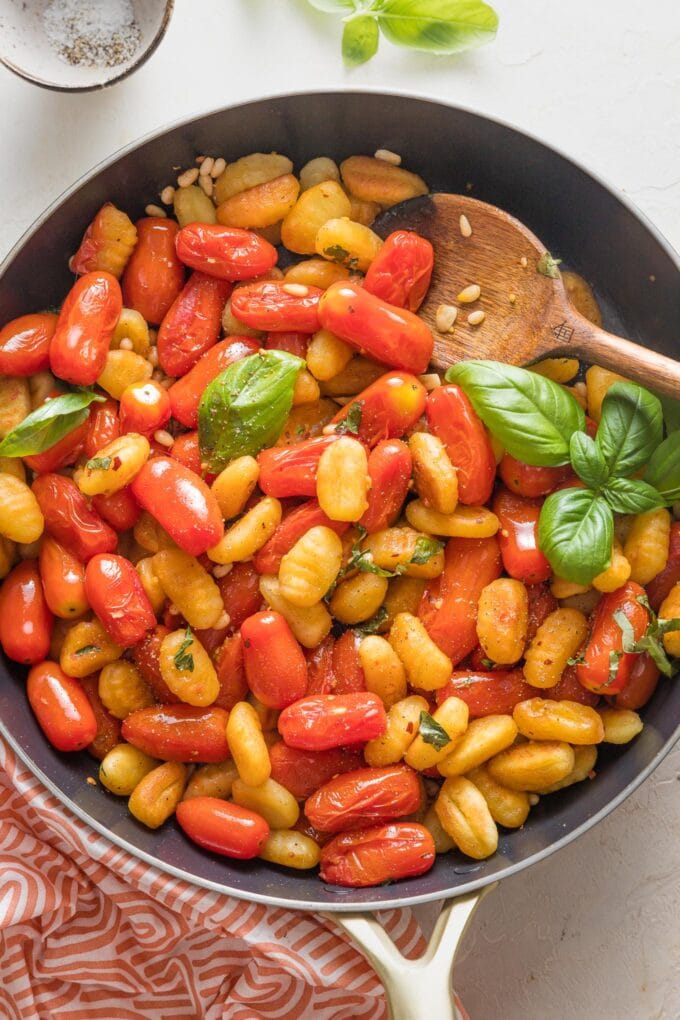 Serving spoon scooping out a portion of pan fried gnocchi with roasted cherry tomatoes and basil.