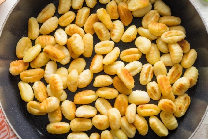 Close up of golden pan-fried gnocchi in a dark skillet.