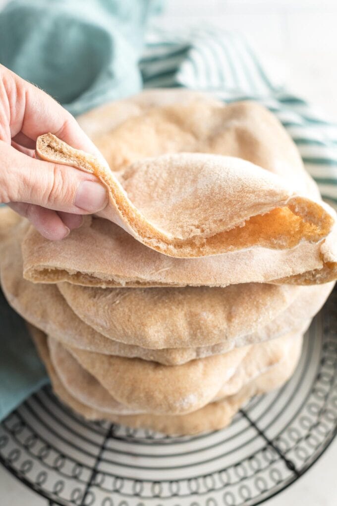 A hand folding up one side of a just-baked pita bread to show that it's soft and pliable.
