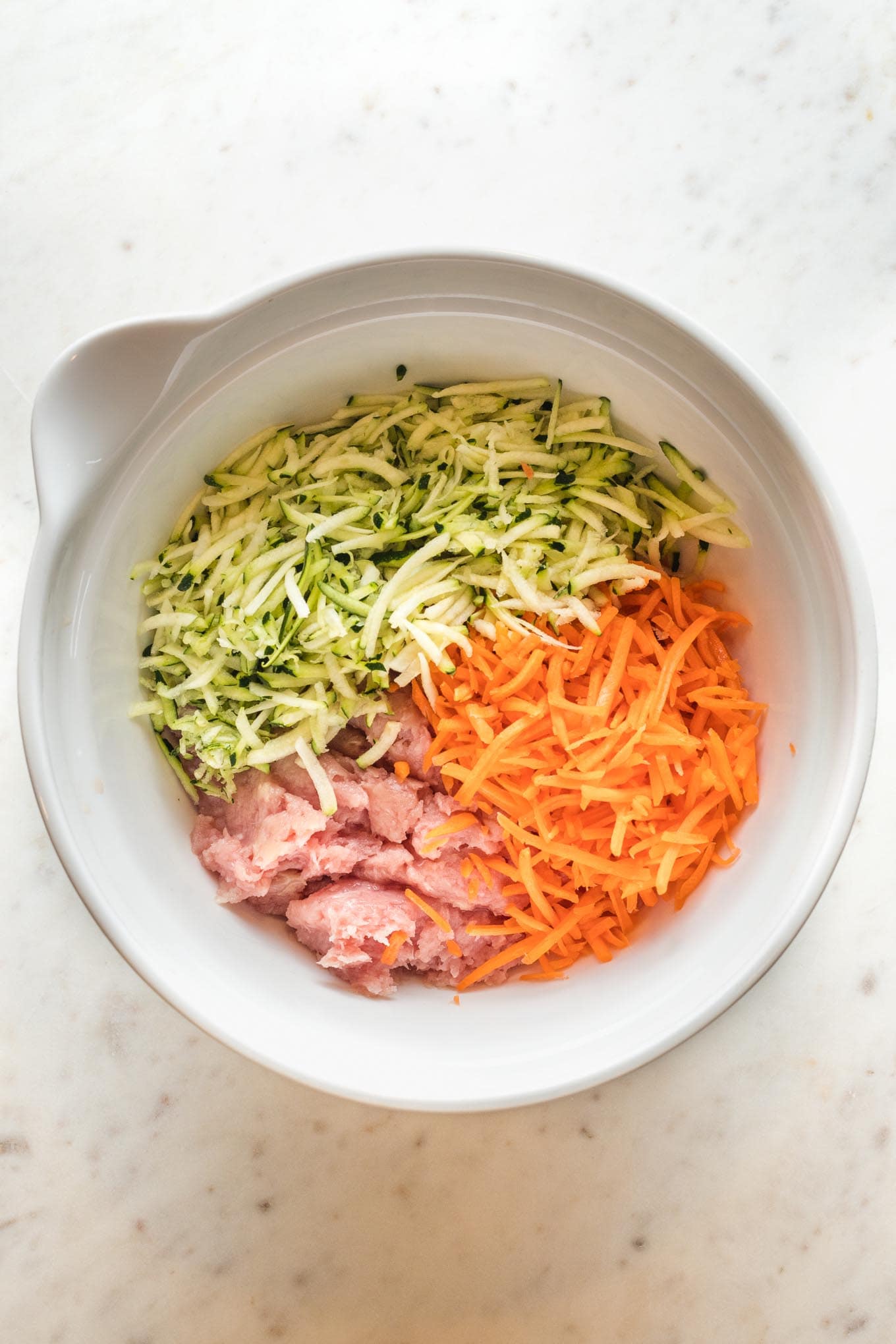 Ground turkey, shredded carrots, and shredded zucchini in a white mixing bowl.