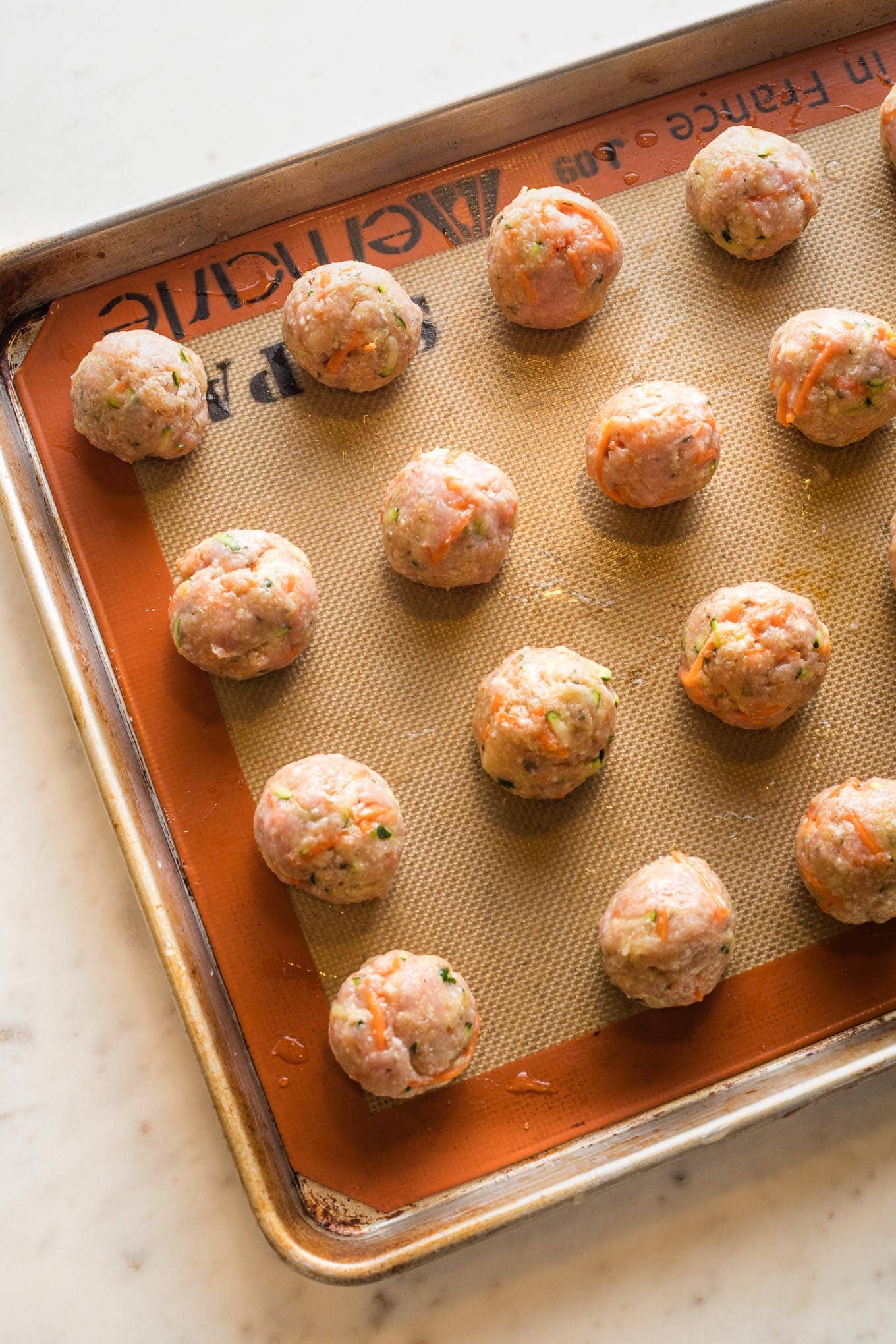 Meatball mixture portioned out and rolled into smooth balls, arranged on a baking tray ready to bake.