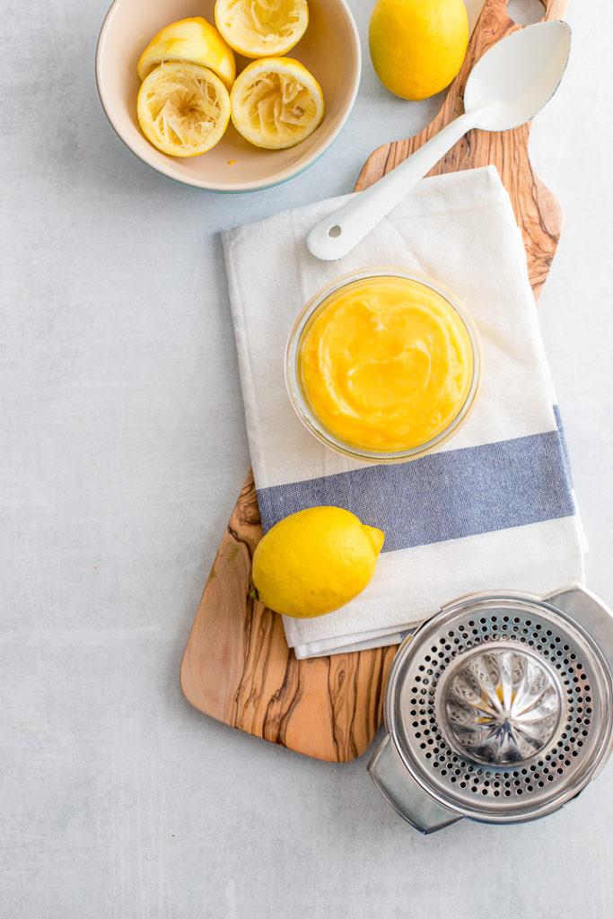 A jar full of bright yellow homemade lemon curd on a white and light blue dishcloth.