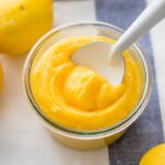 A jar full of bright yellow homemade lemon curd on a white and light blue dishcloth.