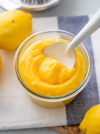 A jar full of bright yellow homemade lemon curd on a white and light blue dishcloth.