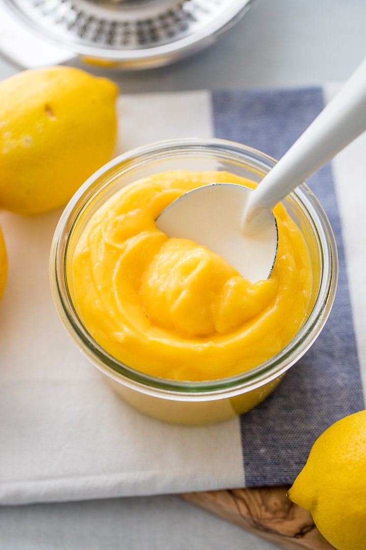 A jar full of bright yellow homemade lemon curd on a white and light blue dishcloth.