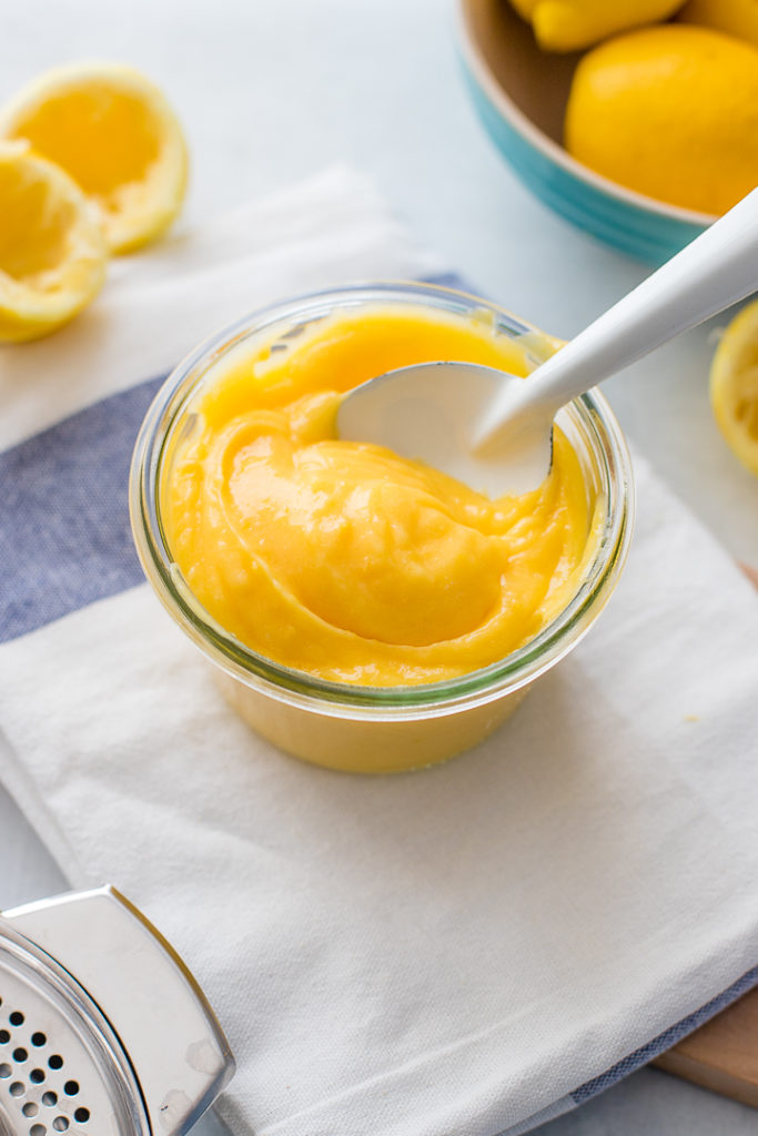 A jar full of bright yellow homemade lemon curd on a white and light blue dishcloth.