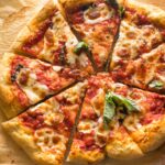 Homemade margherita pizza, fresh out of the oven, sliced and topped with fresh basil.