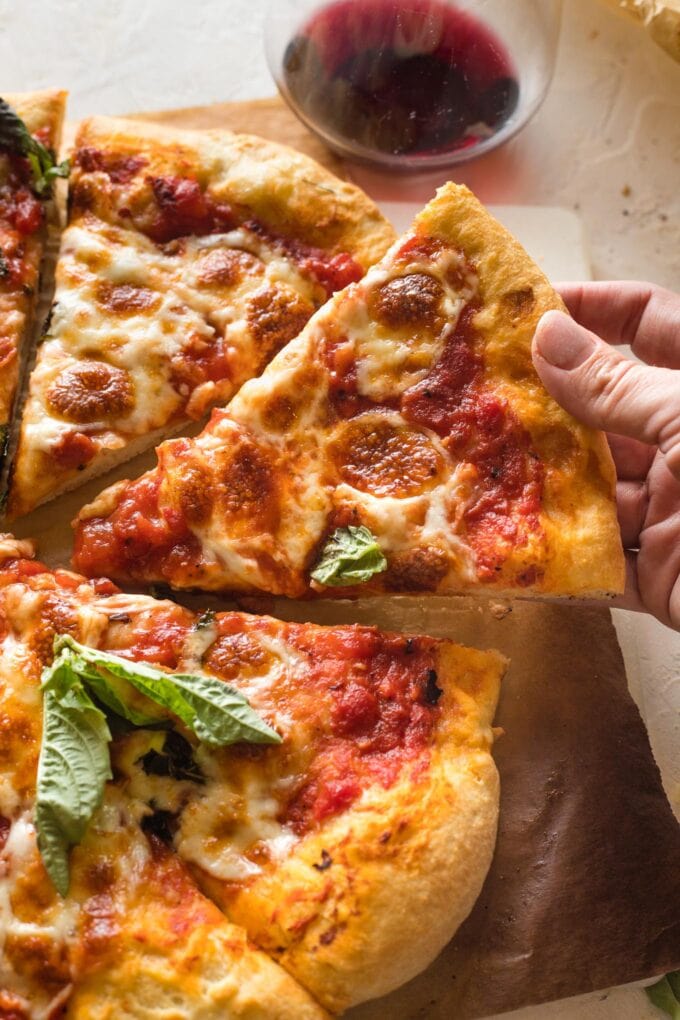 Hand pulling out a slice of homemade margherita pizza.