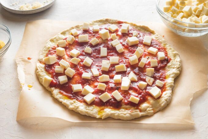 Sauce and cubes of mozzarella cheese spread onto pizza crust.