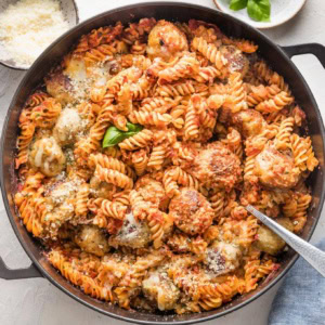 Large cast iron skillet with a chicken Parmesan pasta bake made of meatballs, pasta, and a simple homemade tomato sauce.
