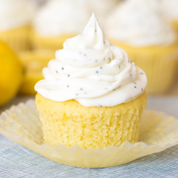 Close up of a lemon cupcake topped with a generous swirl of cream cheese frosting with poppyseeds mixed in.