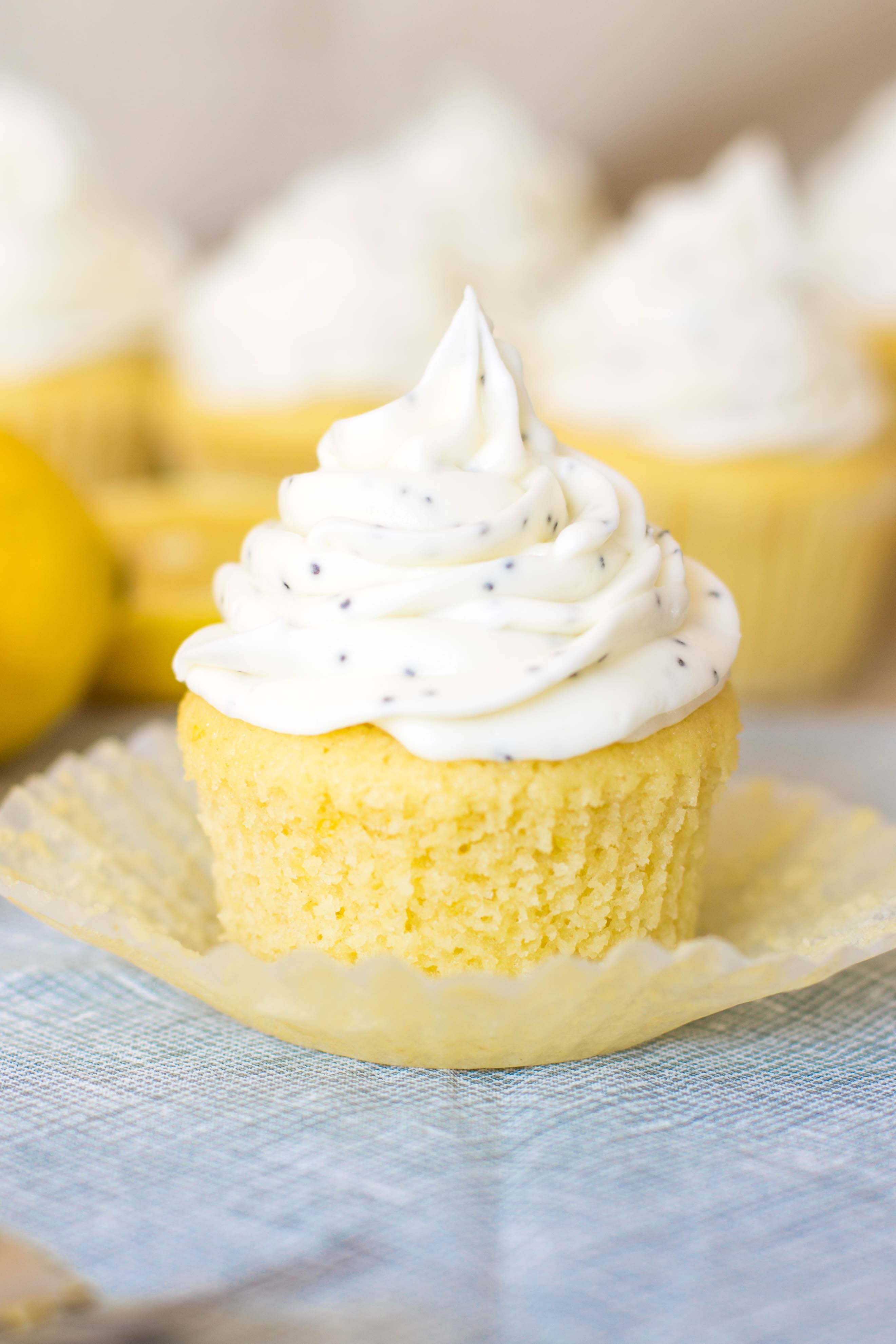 Close up of a lemon cupcake topped with a generous swirl of cream cheese frosting with poppyseeds mixed in.