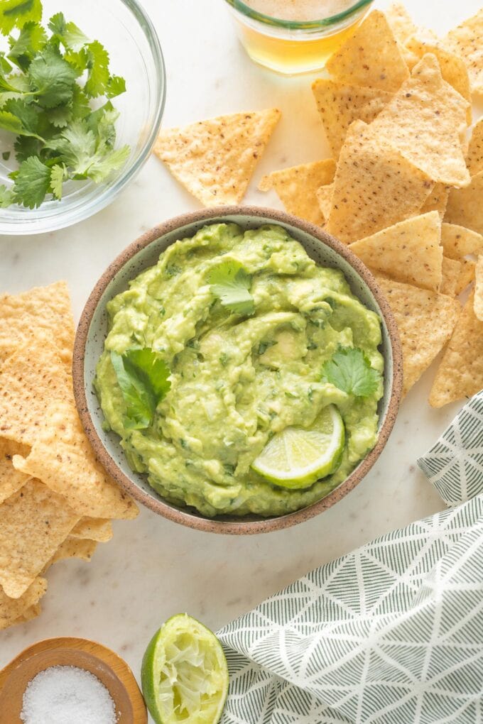 Bowl of homemade guacamole surrounded by tortilla chips and an ice cold beer in a glass.