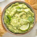 Small bowl of guacamole garnished with lime wedges and cilantro.