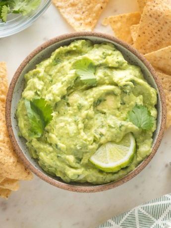 Small bowl of guacamole garnished with lime wedges and cilantro.